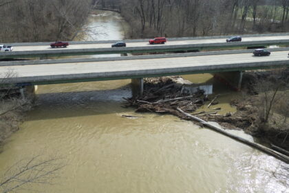 Bridge over river with cars driving across and trees dammed at the pile.