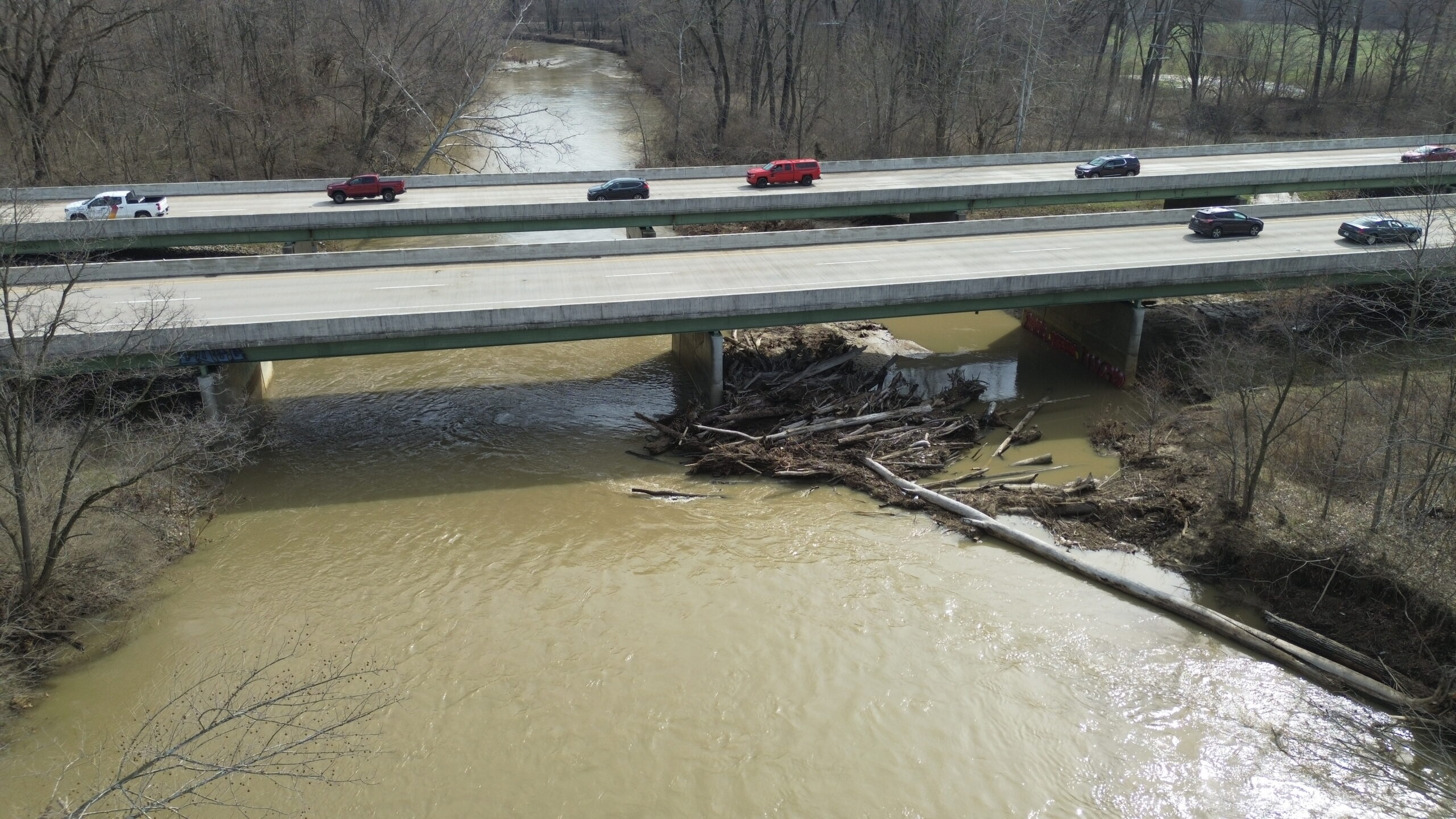 Bridge over river with cars driving across and trees dammed at the pile.