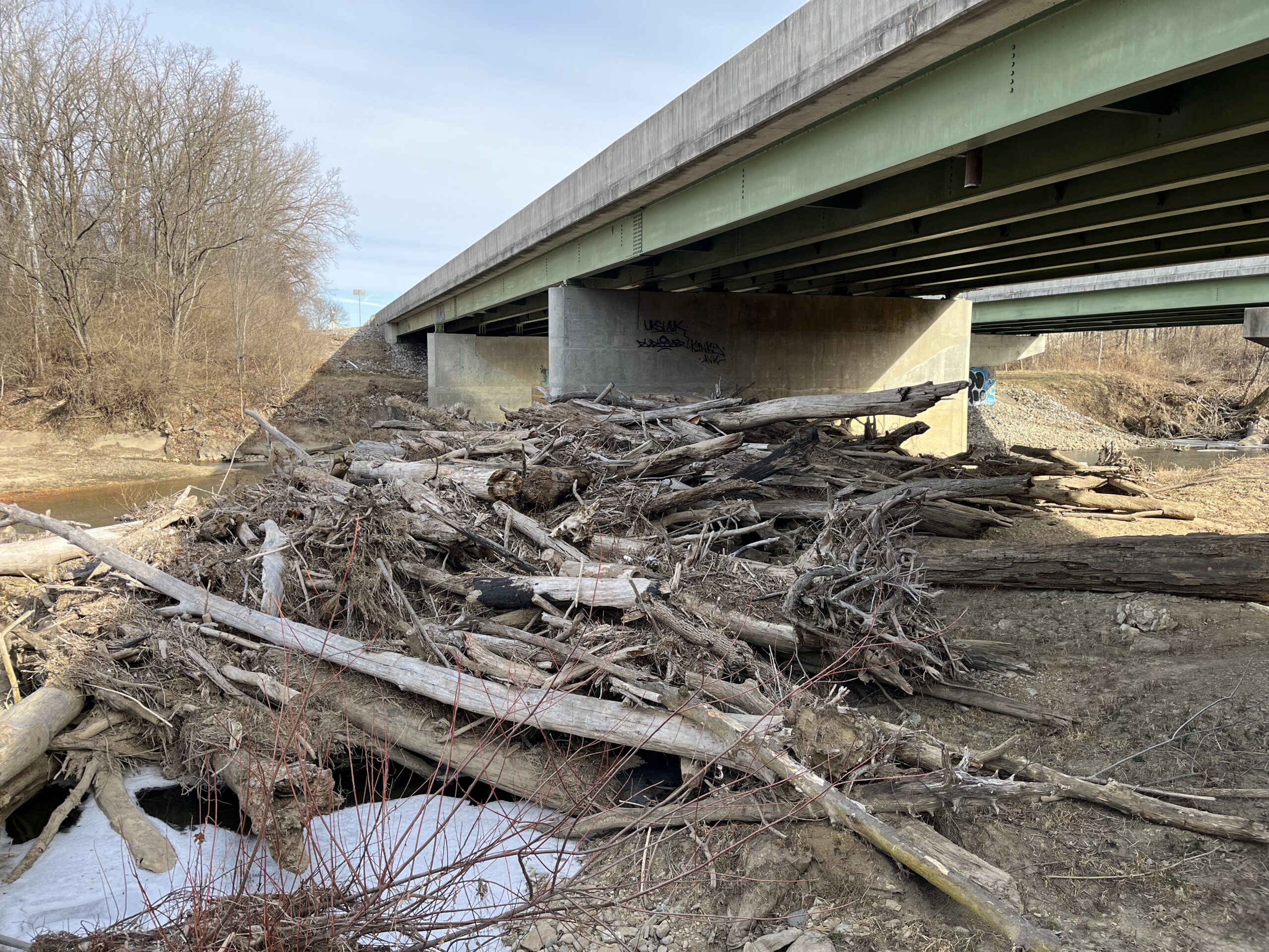 Pile of logs and debris dammed up below a bridge.